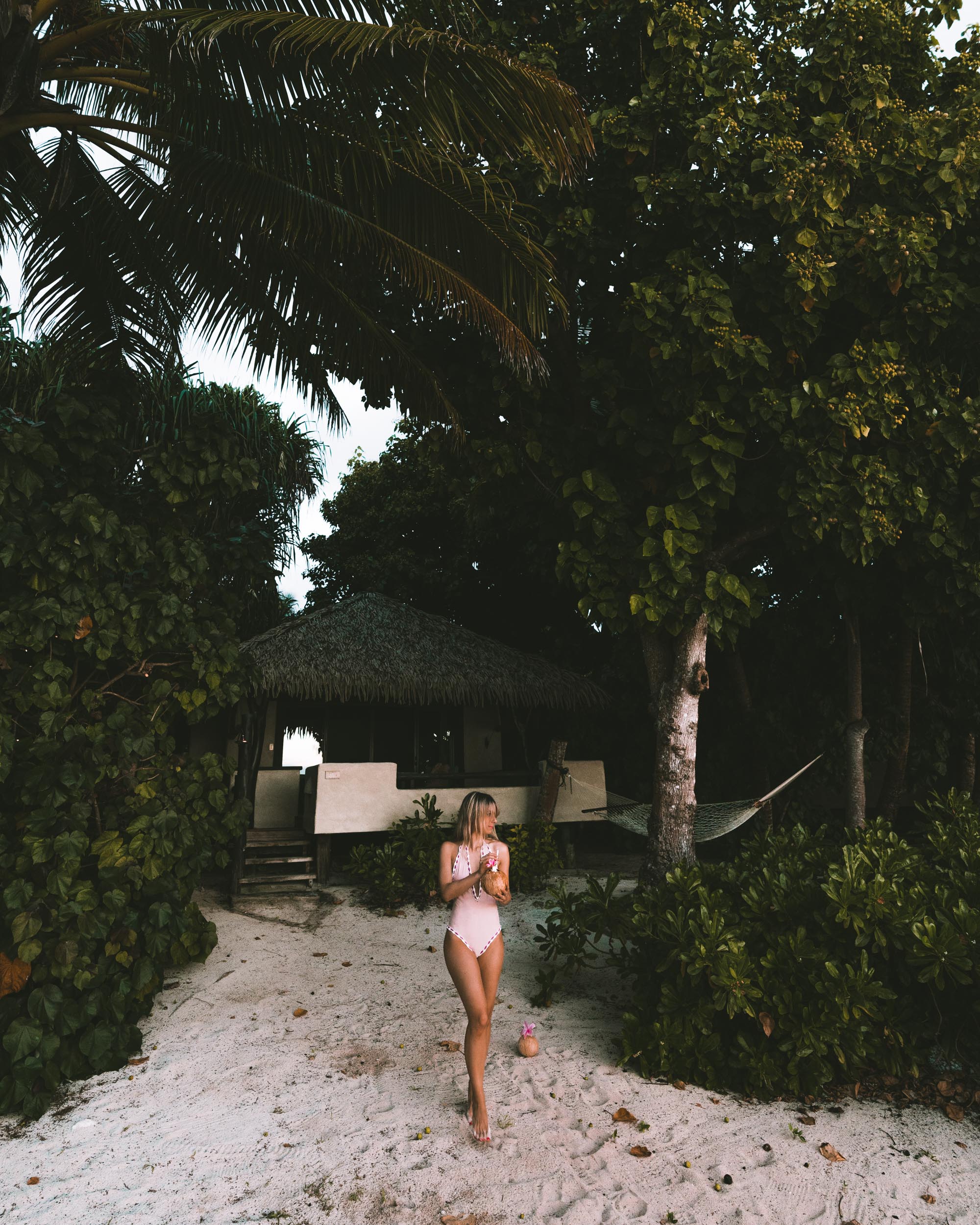Travel blogger Selena Taylor in a pink swimsuit in front of a bungalow in the beach in Aitutaki, Cook Islands